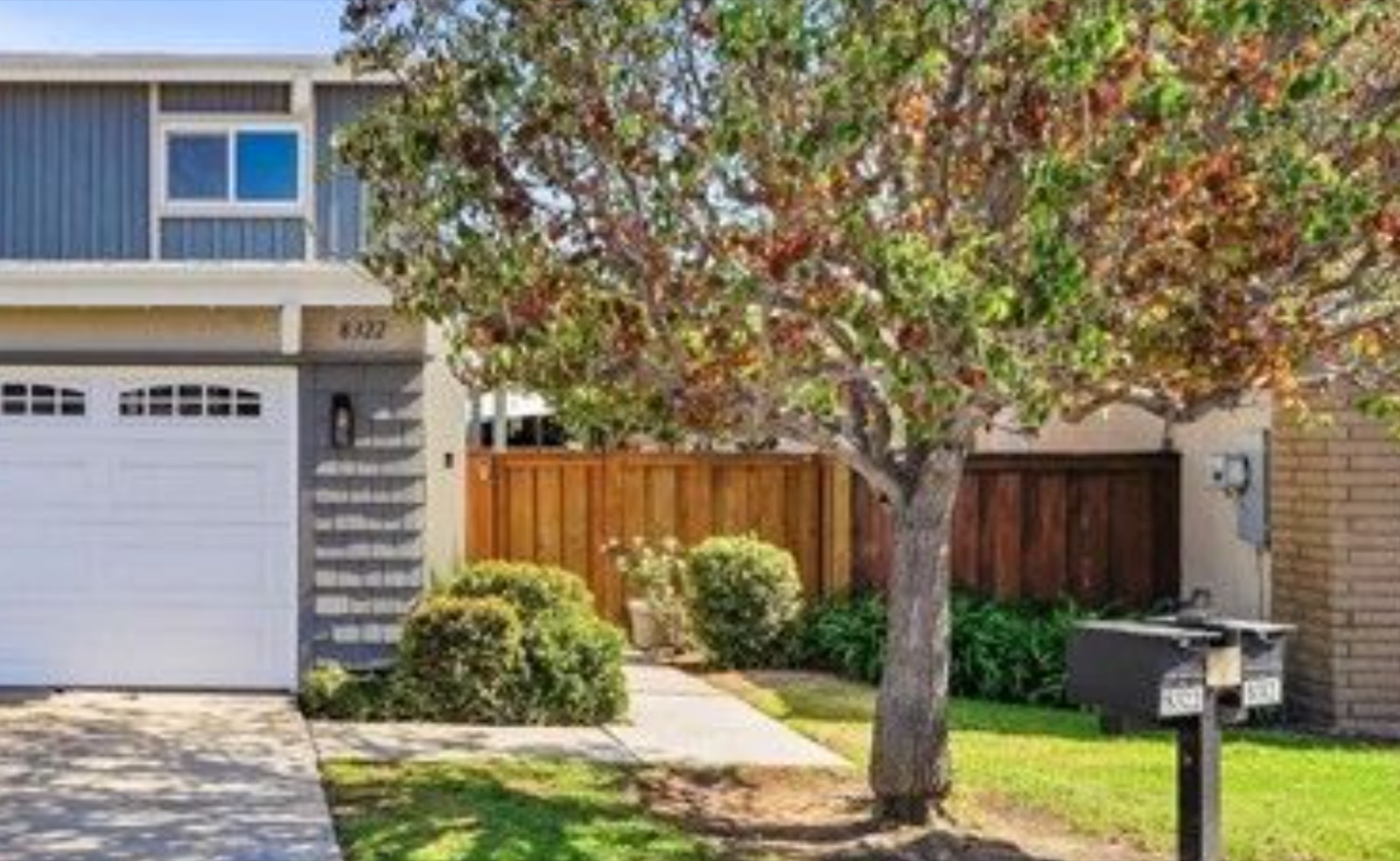 Front exterior of 8322 Padrino, an end-unit townhome in Huntington Beach with a two-car garage and mature shade tree